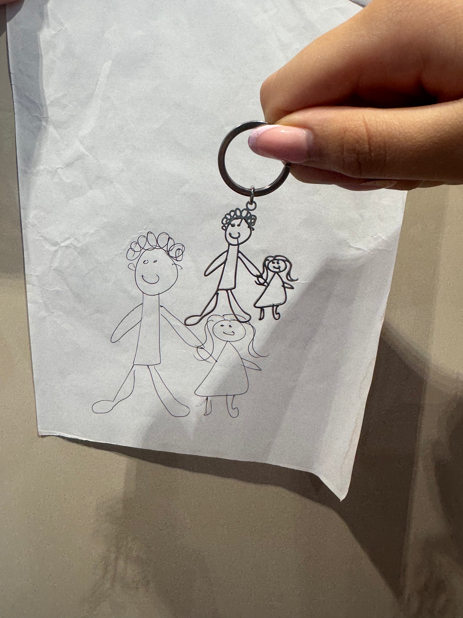 A personalised keyring held in front of the child’s original drawing